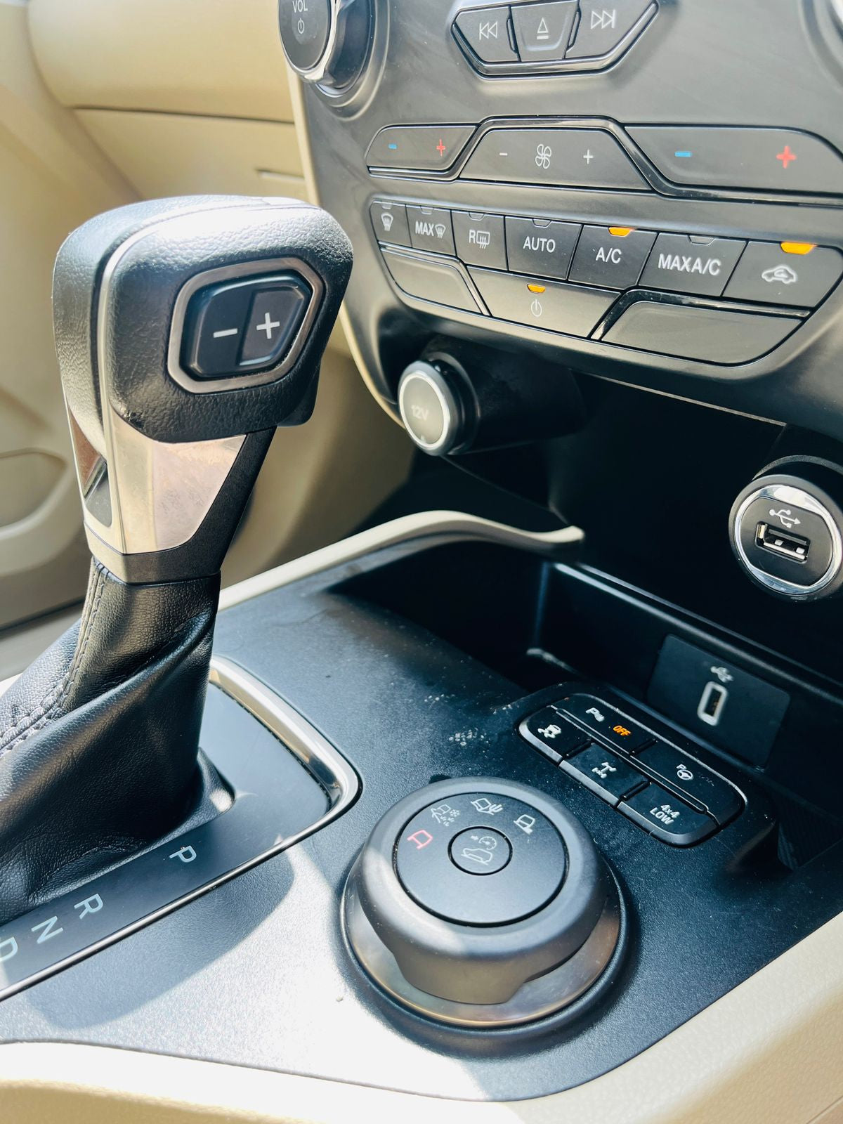 Close-up of a car's gear shift and control panel with beige interior.