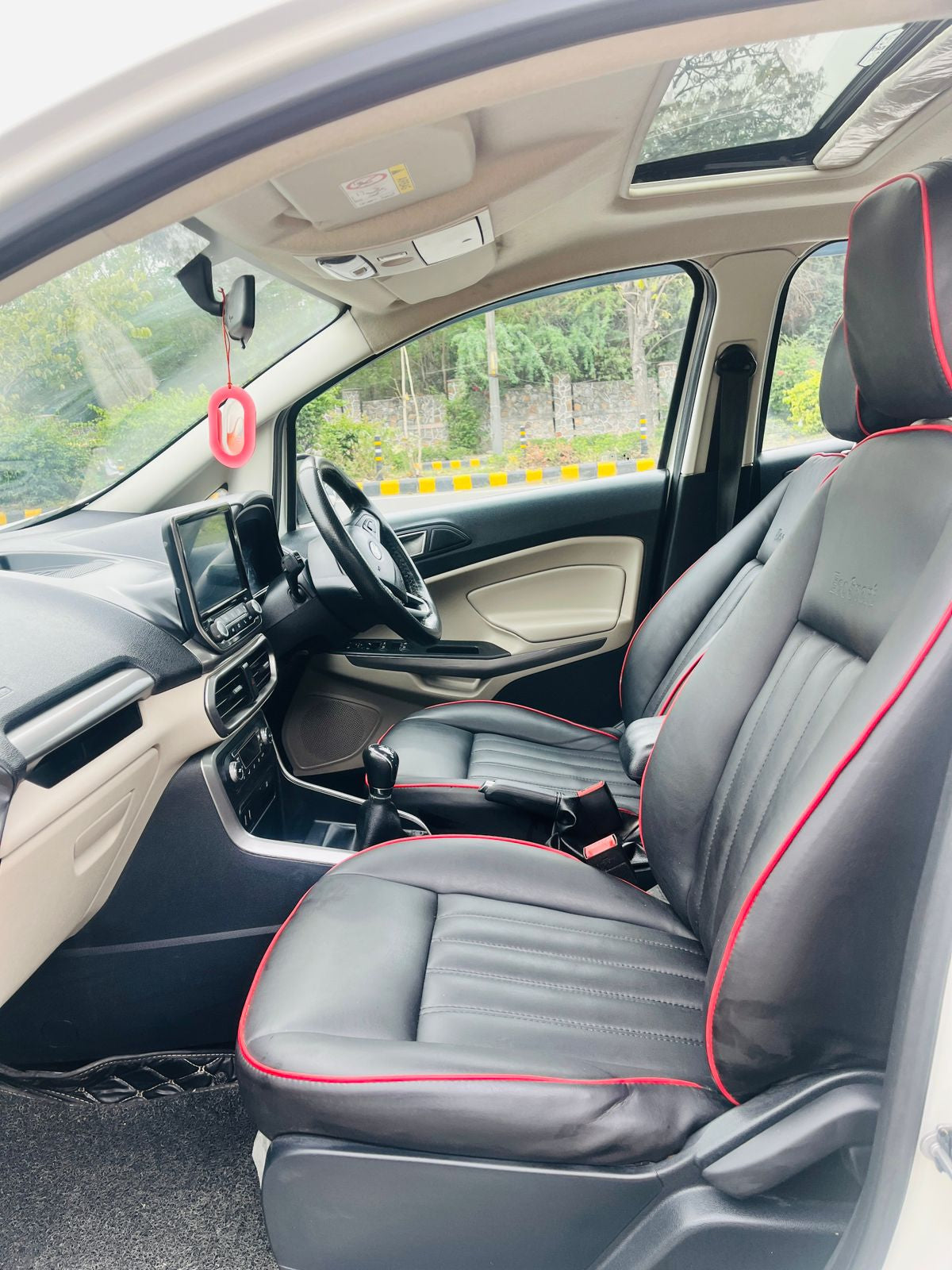 Car interior with black leather seats and red stitching, showing dashboard and steering wheel.