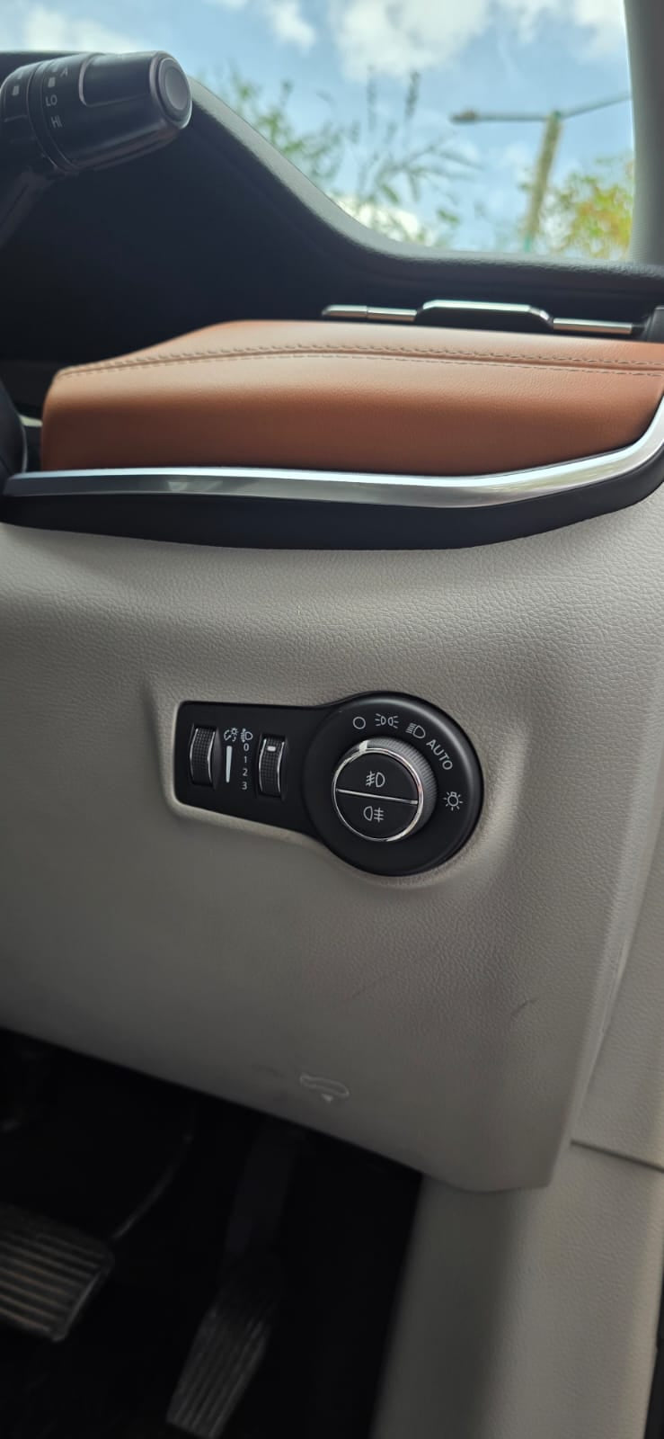 Car interior panel with control buttons and brown leather armrest.
