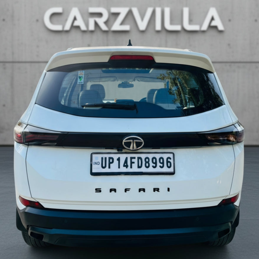White SUV with 'Tata' logo and 'Safari' model name, parked in front of a 'CARZVILLA' sign.