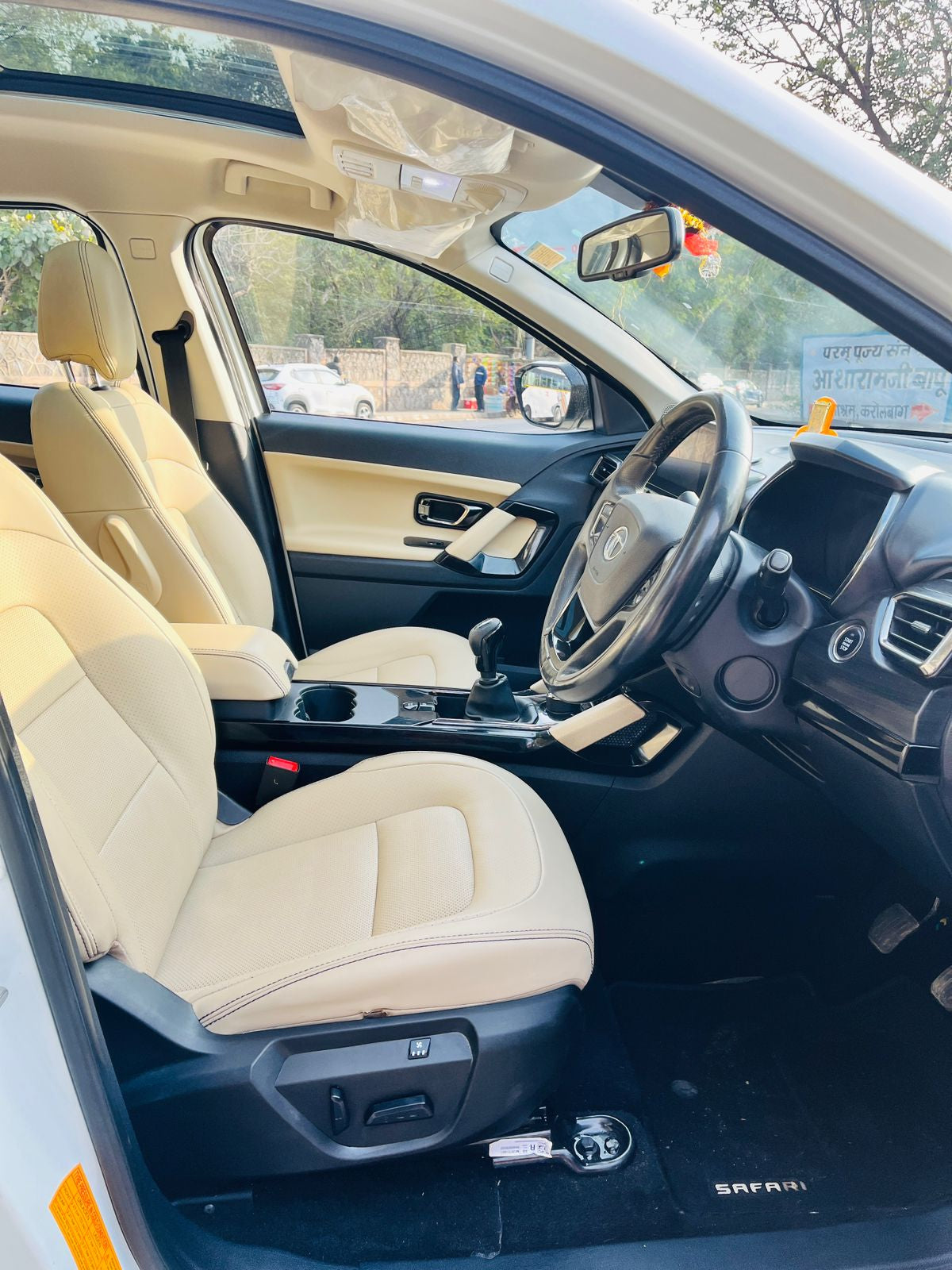 Car interior with beige seats and steering wheel, visible through a car window.