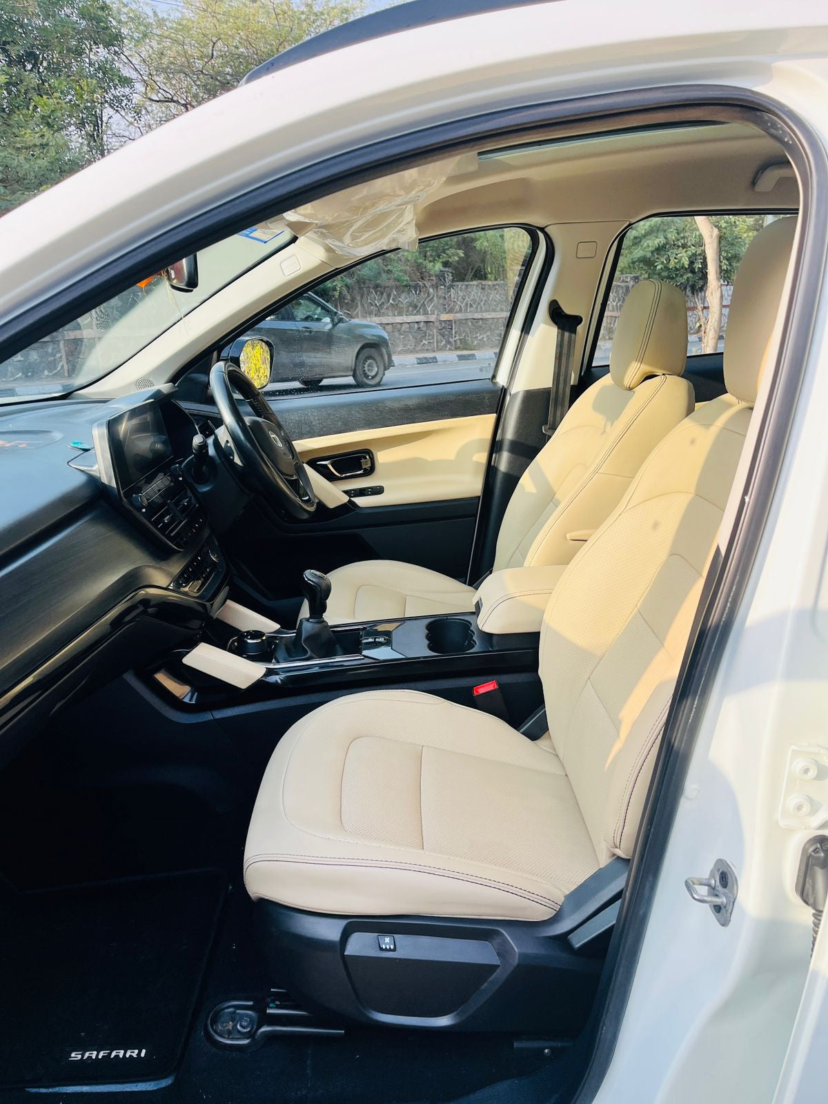 Car interior with beige seats and dashboard, showing a view of the road outside.