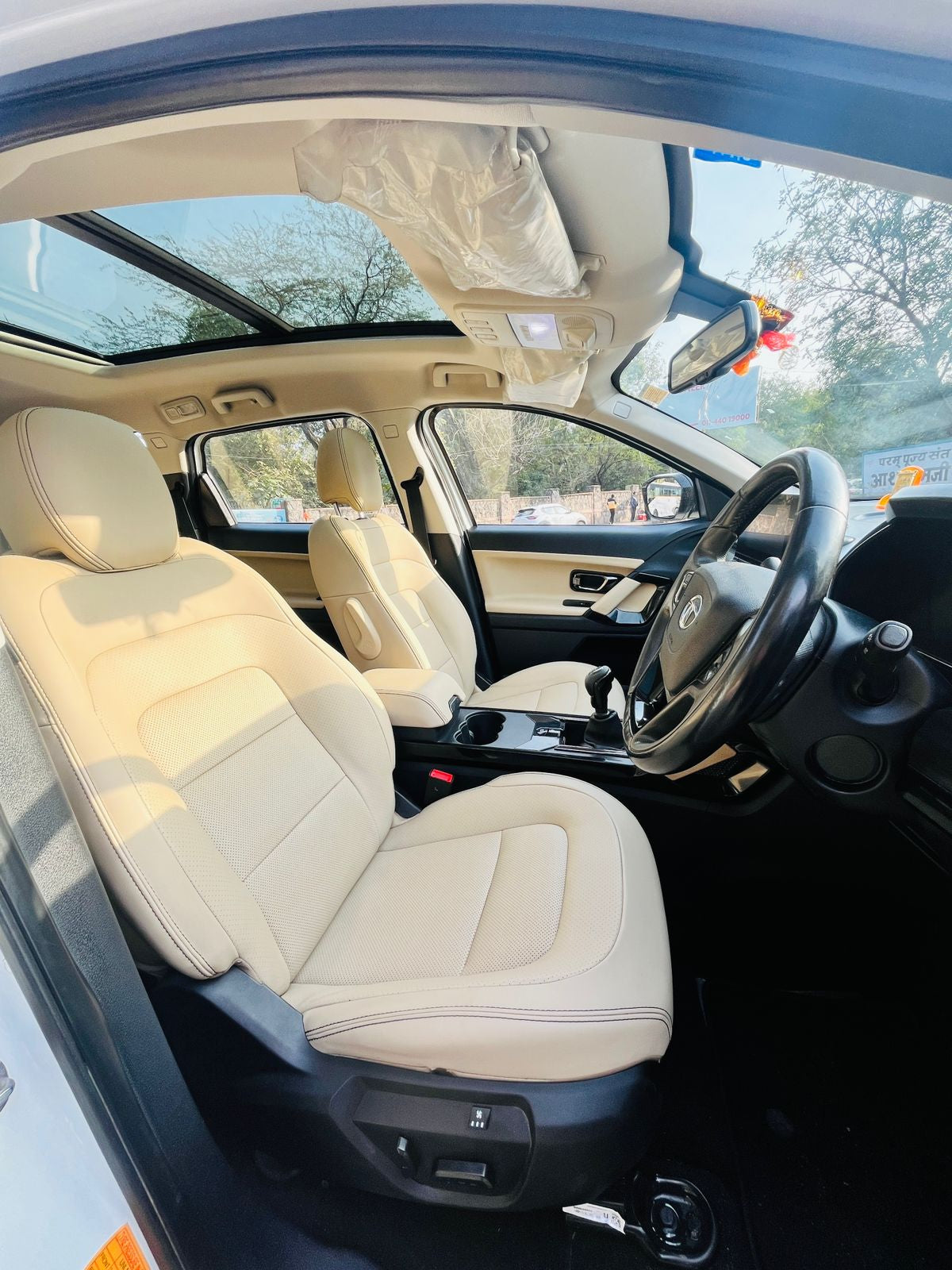 Car interior with beige seats and a steering wheel, showing a clear sky outside.