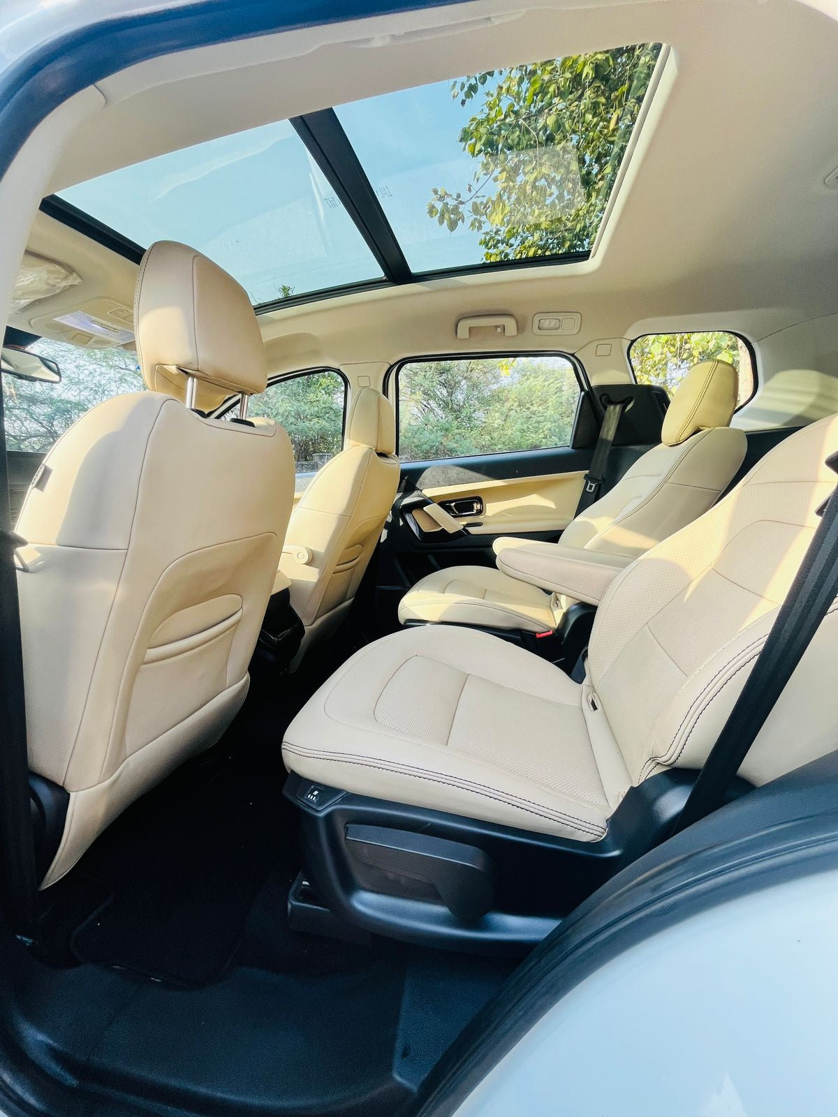 Beige interior of a car with a panoramic sunroof, showing clear blue sky and greenery outside.
