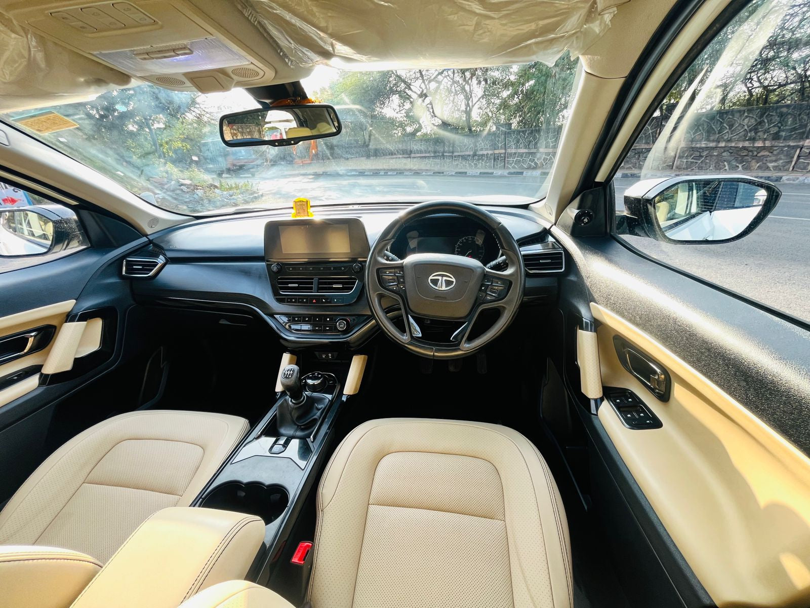 Car interior with beige seats and dashboard, showing the steering wheel and controls.