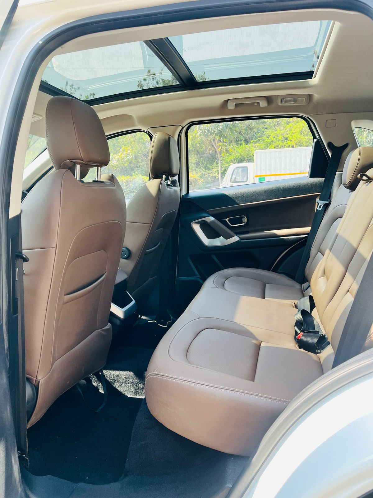 Beige interior of a car with sunroof and open door, showing rear seats.