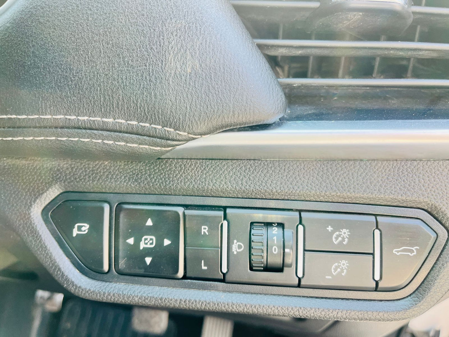 Car interior control panel with various buttons on a gray dashboard.