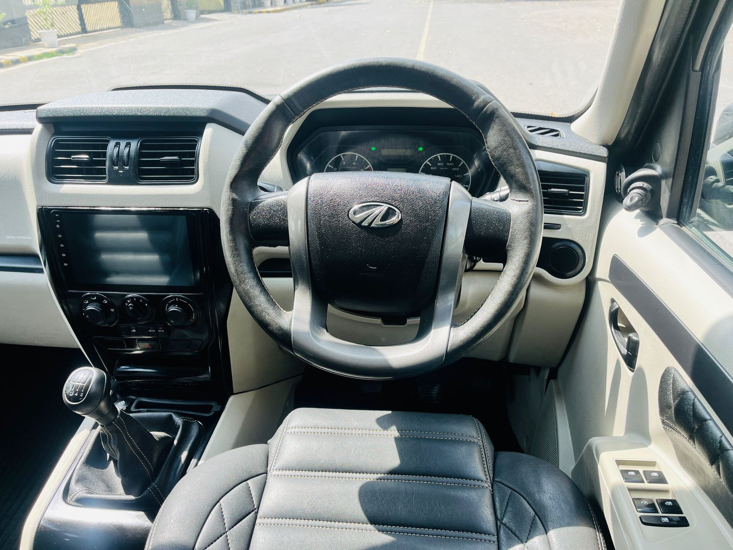 Car interior with steering wheel featuring a logo, dashboard, and seats.