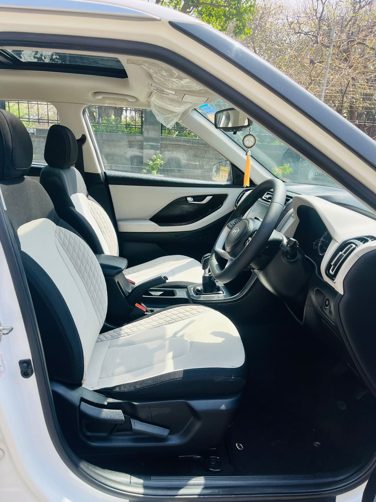 Car interior with white seats and black steering wheel, visible through a car window.