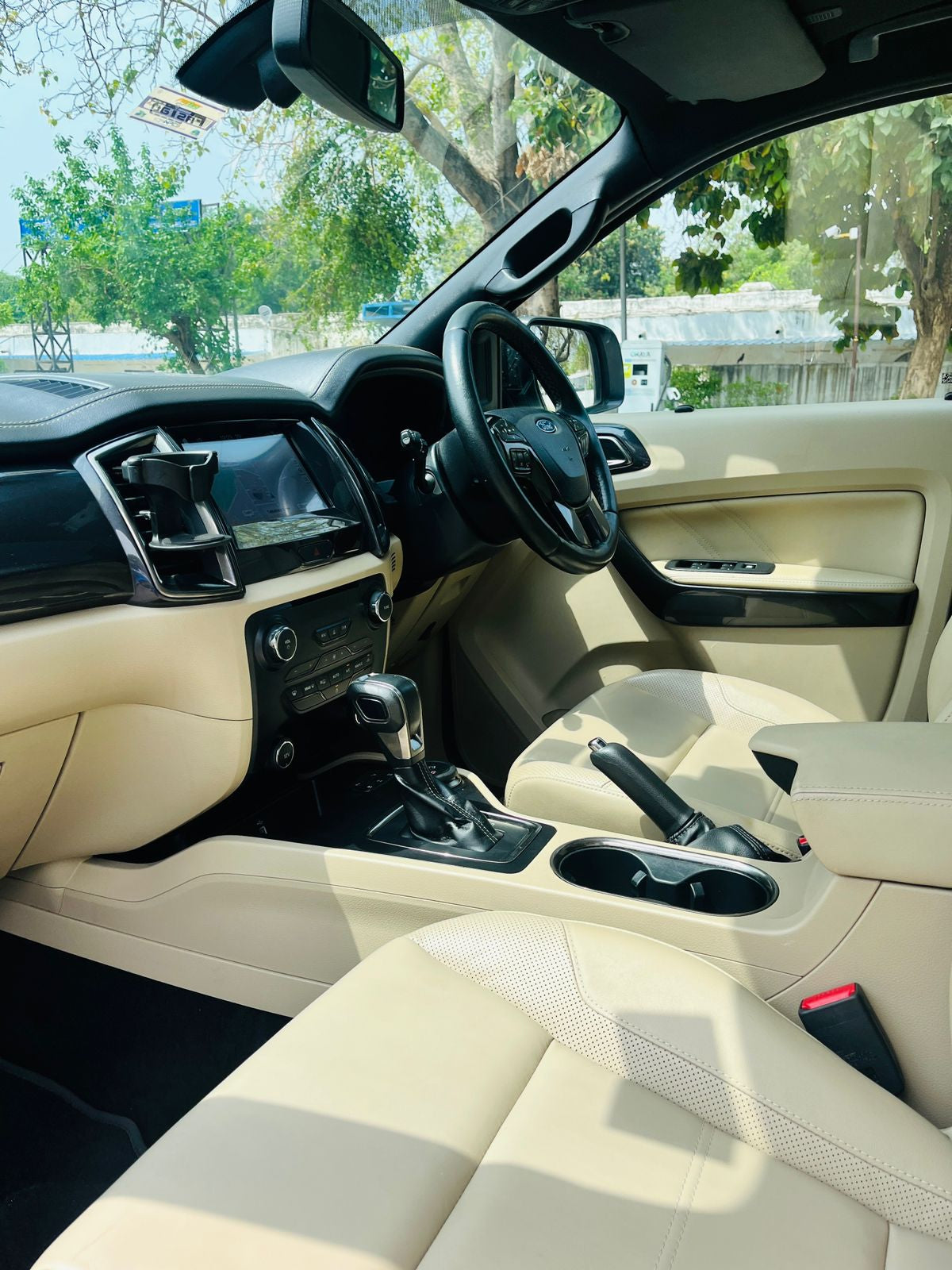Car interior with beige leather seats and dashboard, showing steering wheel and controls.