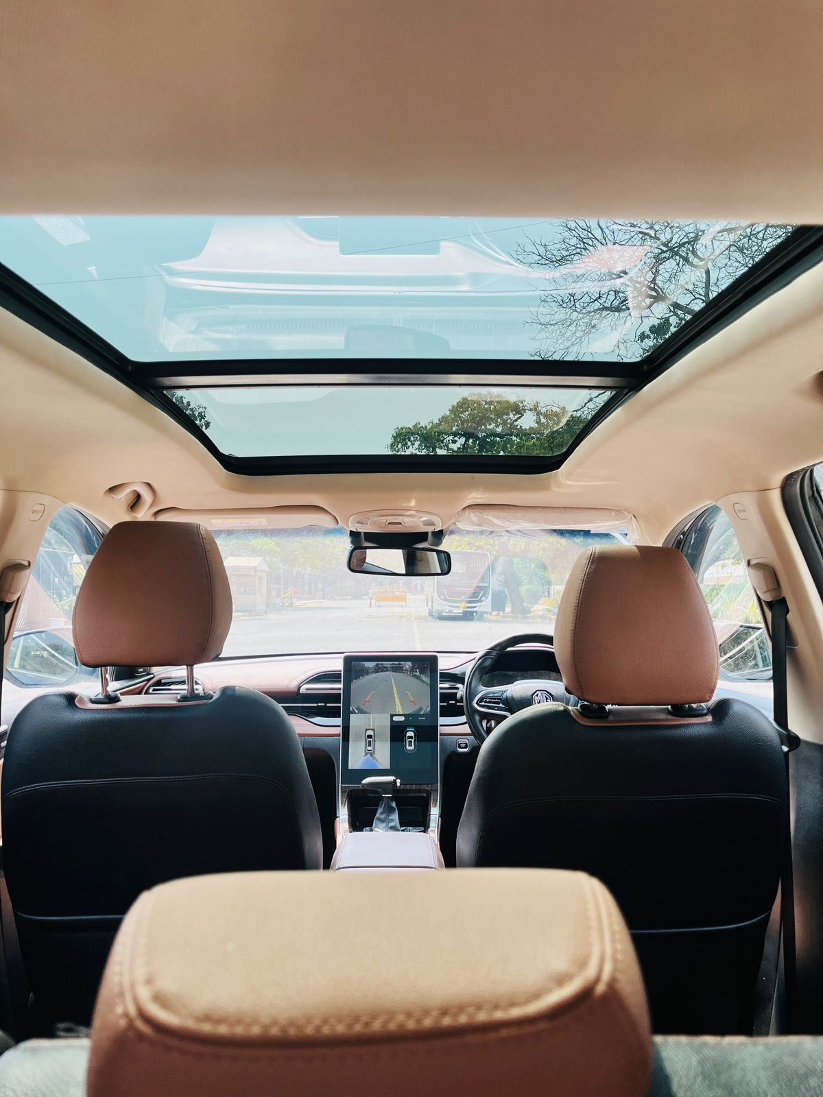 Car interior with a sunroof and a view of trees and sky outside.