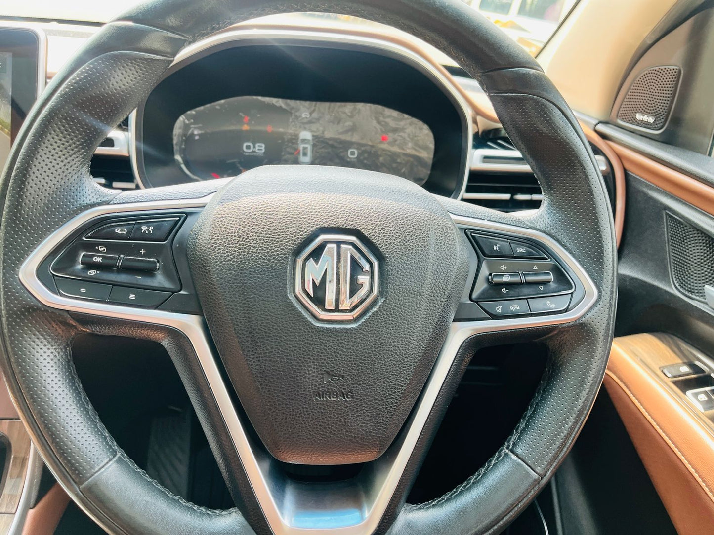 Steering wheel of a car with MG logo, showing dashboard and interior details.