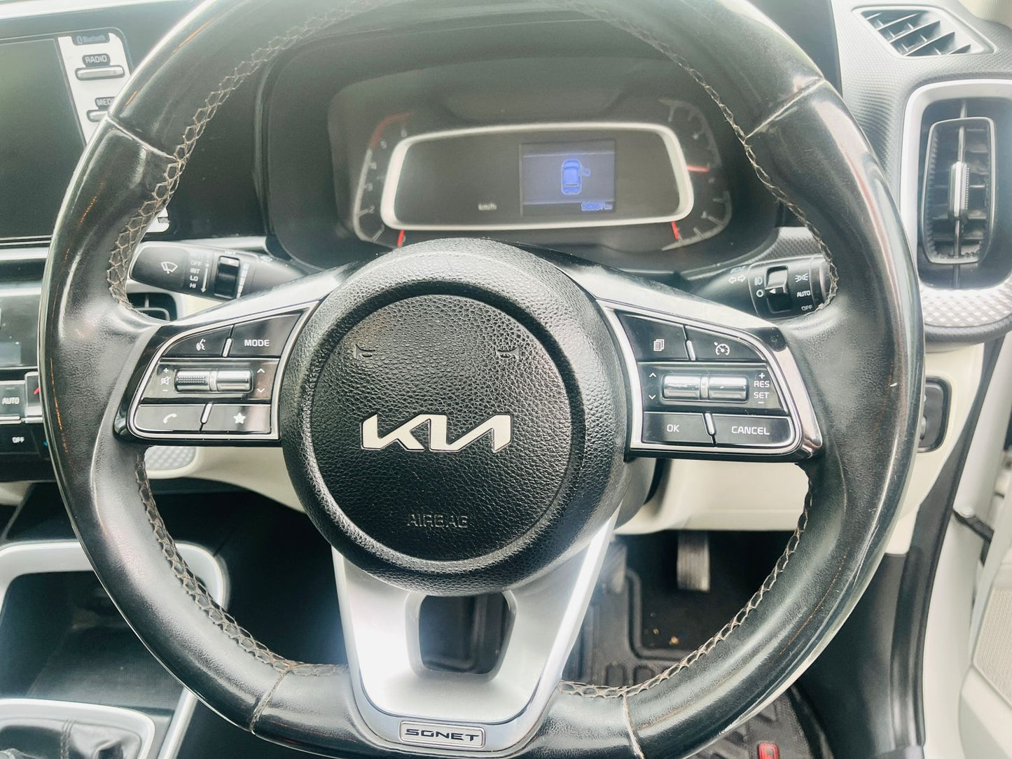 Steering wheel of a Kia vehicle with dashboard in the background