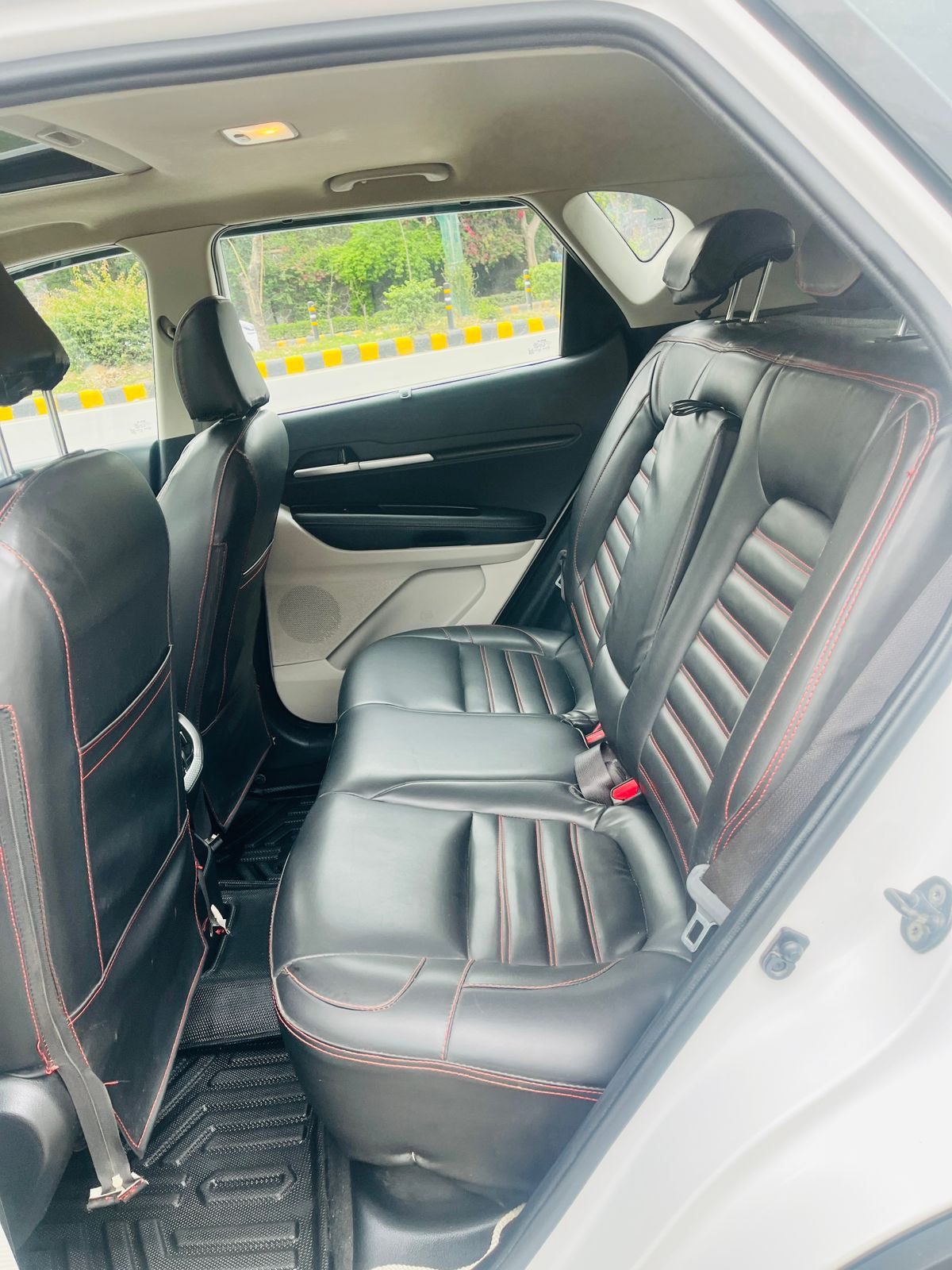 Back seat of a car with black leather seats and red stitching.