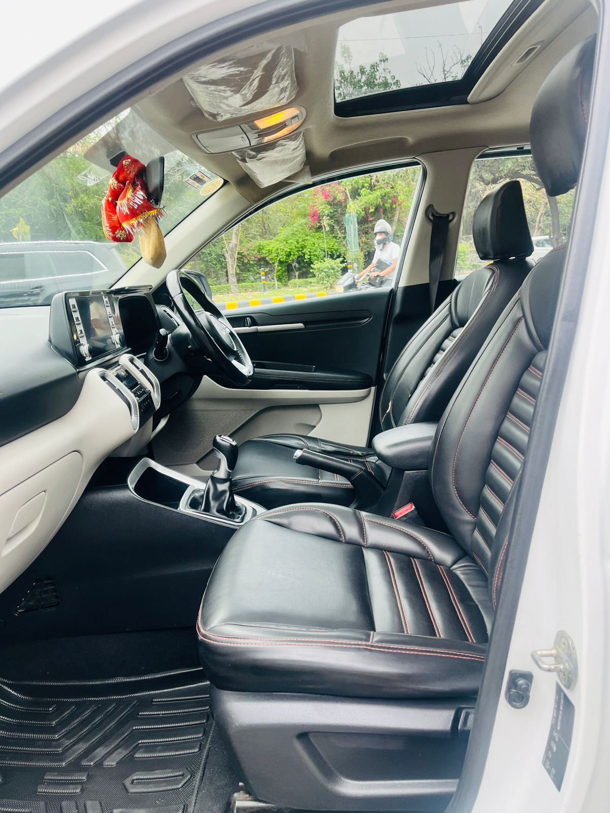 Car interior with black leather seats and dashboard, showing a person outside the car.