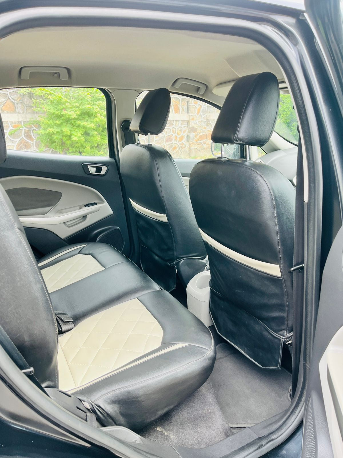 Car interior with black leather seats and open door showing outdoor view.