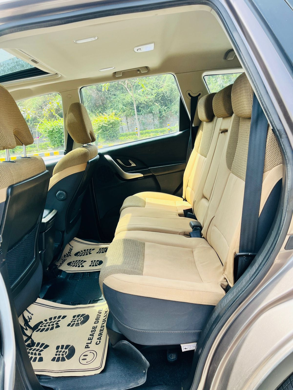 Beige car interior with open door, showing rear seats and floor mat.
