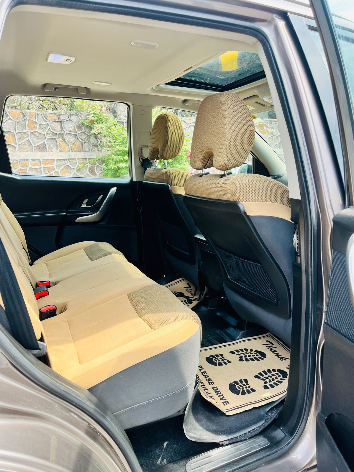 Car interior with beige seats and open door showing a stone wall and greenery outside.