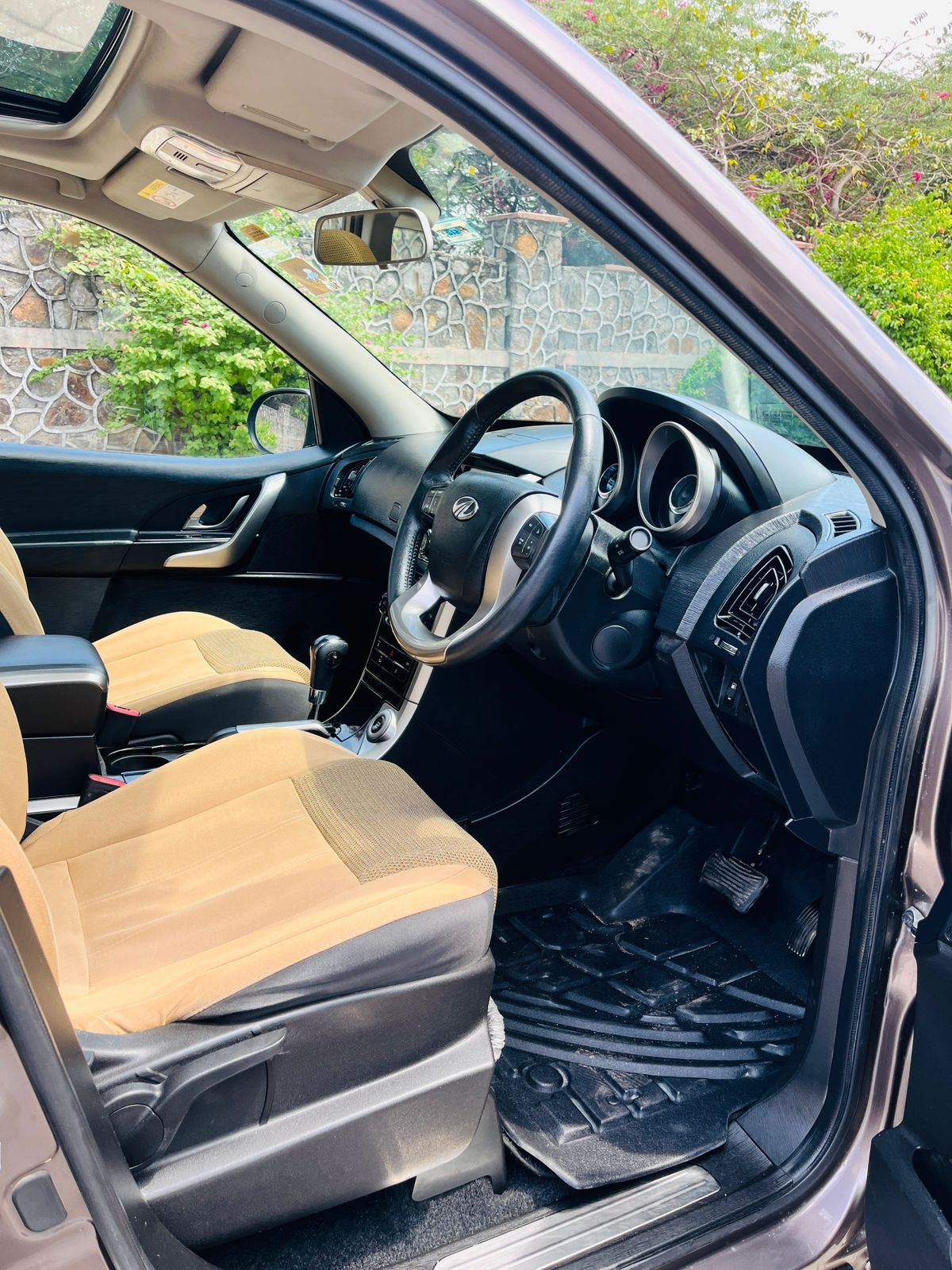 Car interior with beige seats and steering wheel, visible through a window.
