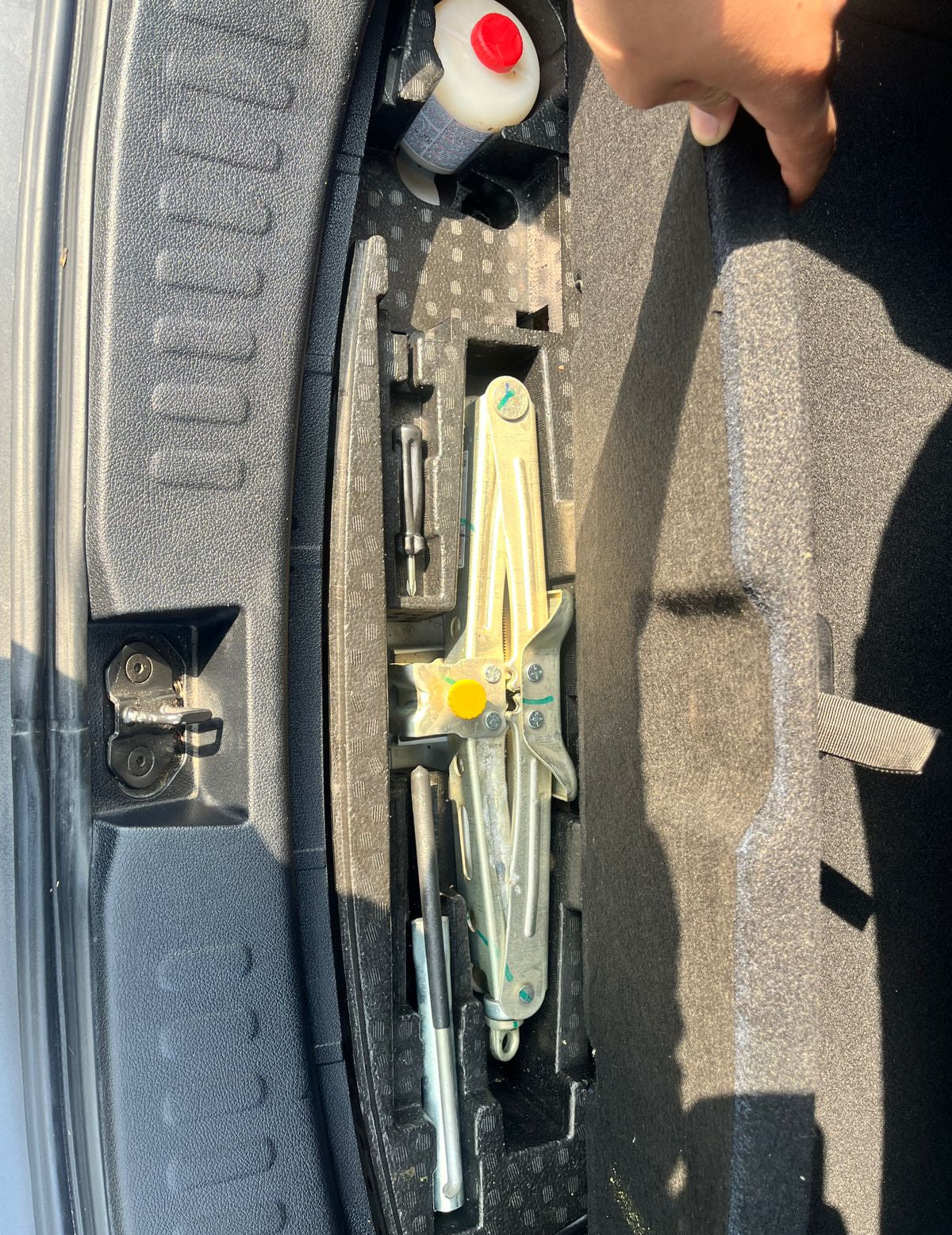 Car trunk with tools and a bottle of liquid, possibly for maintenance or repair.