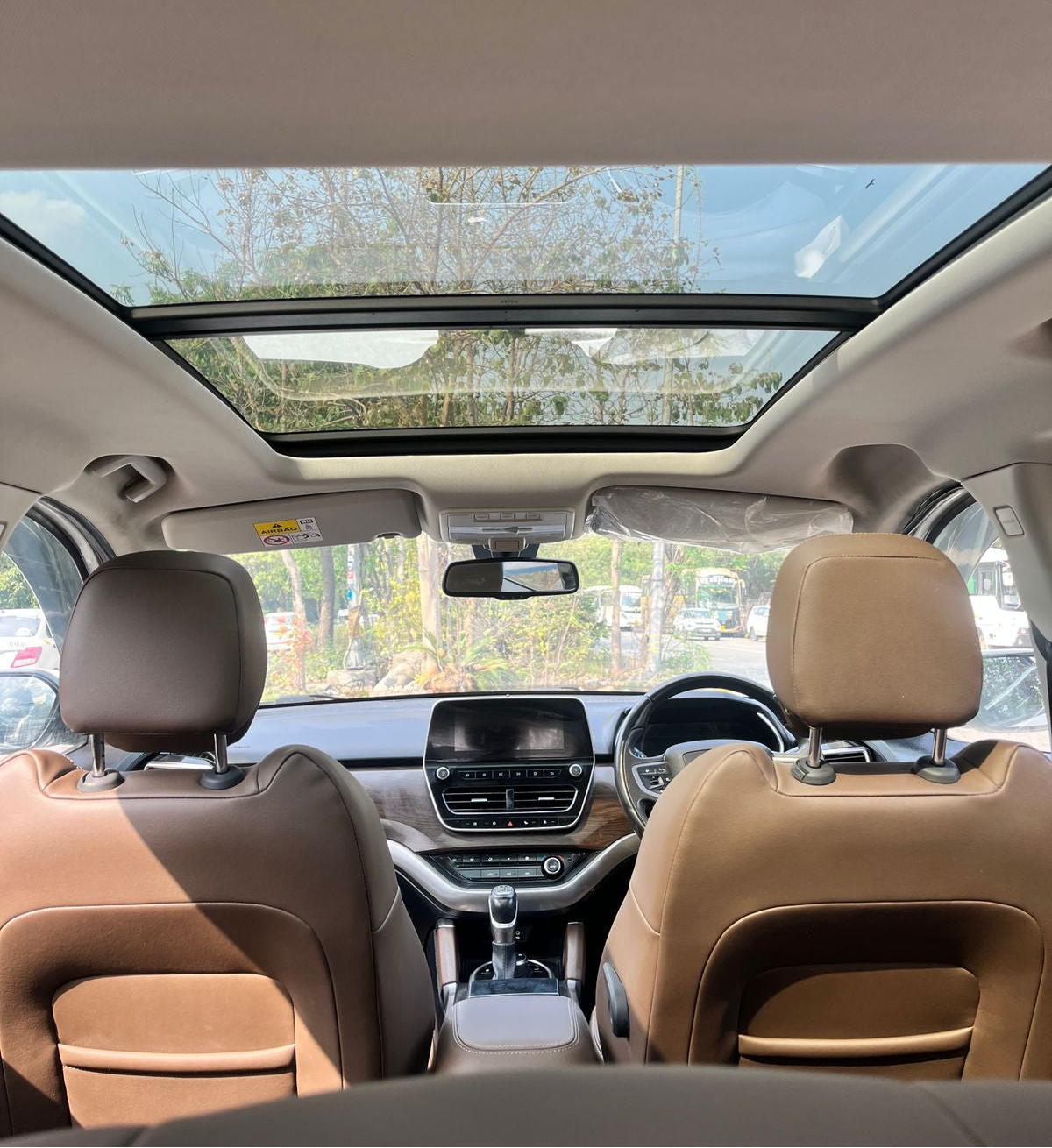 Car interior with beige leather seats and a sunroof, showing a view of trees outside.
