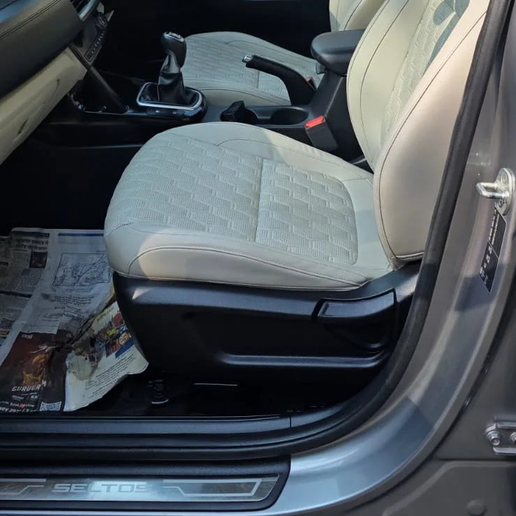 Car interior with beige seats and dashboard, open car door showing newspaper on floor.
