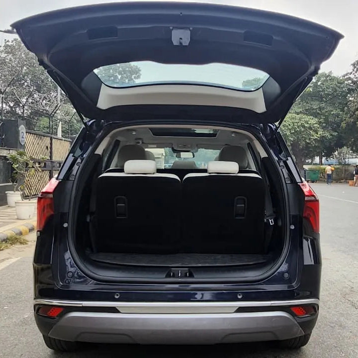 SUV with open trunk on a road with trees and buildings in the background