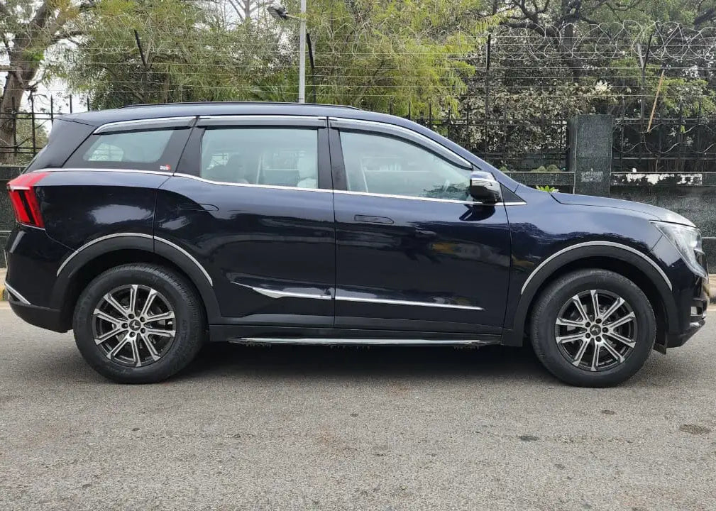 Black SUV parked on a road with trees and a wall in the background