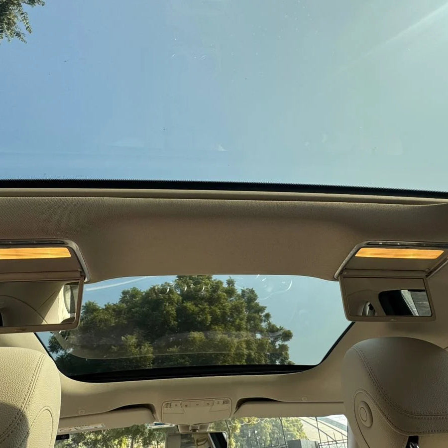 Car interior with sunroof open, showing a clear blue sky and trees outside.