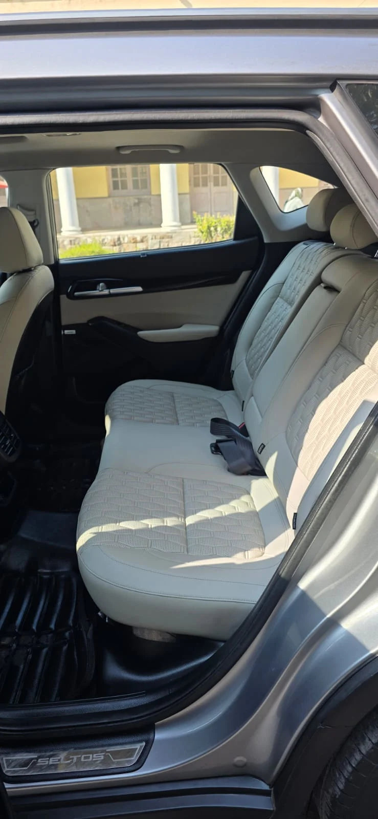 Car interior with beige seats and open door showing exterior.