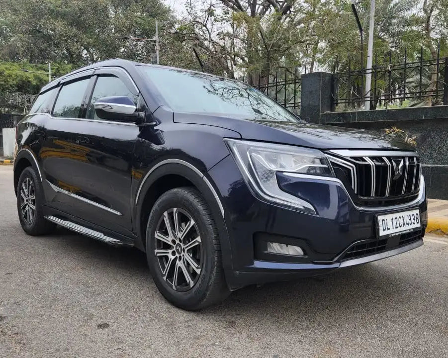 Blue SUV parked on a road with trees and a wall in the background