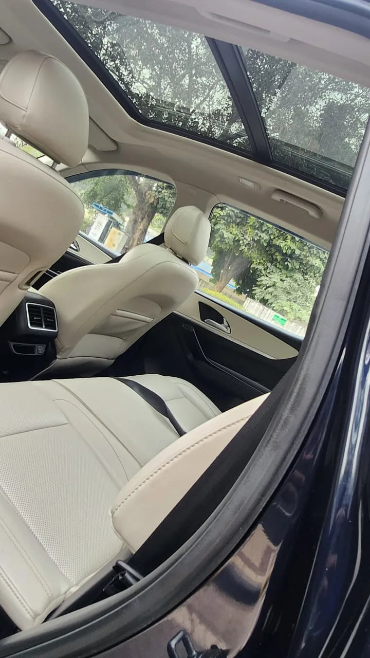 Car interior with beige seats and a sunroof, showing a view of trees outside.